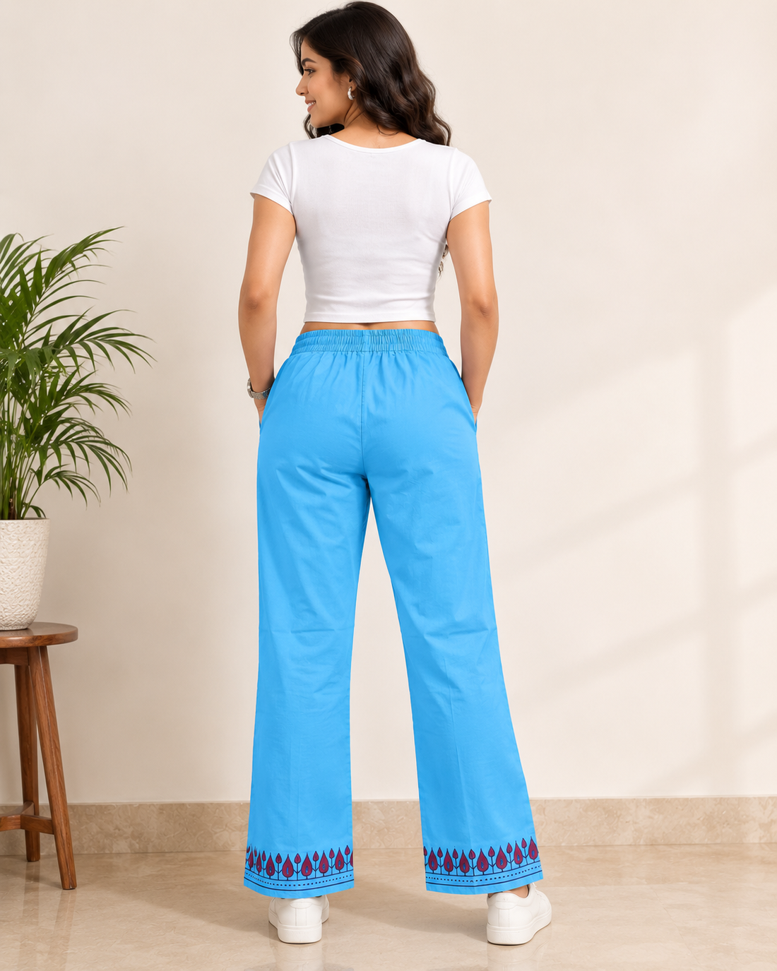 A woman modeling bright blue wide-leg pajama pants with a white crop top and white sneakers against a plain beige studio background.