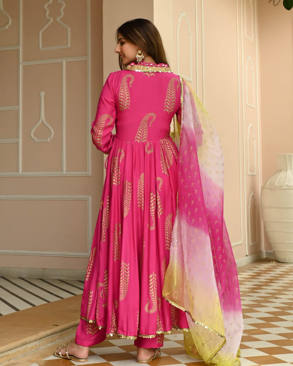 Woman in a pink traditional outfit with gold patterns in an elegant interior setting.