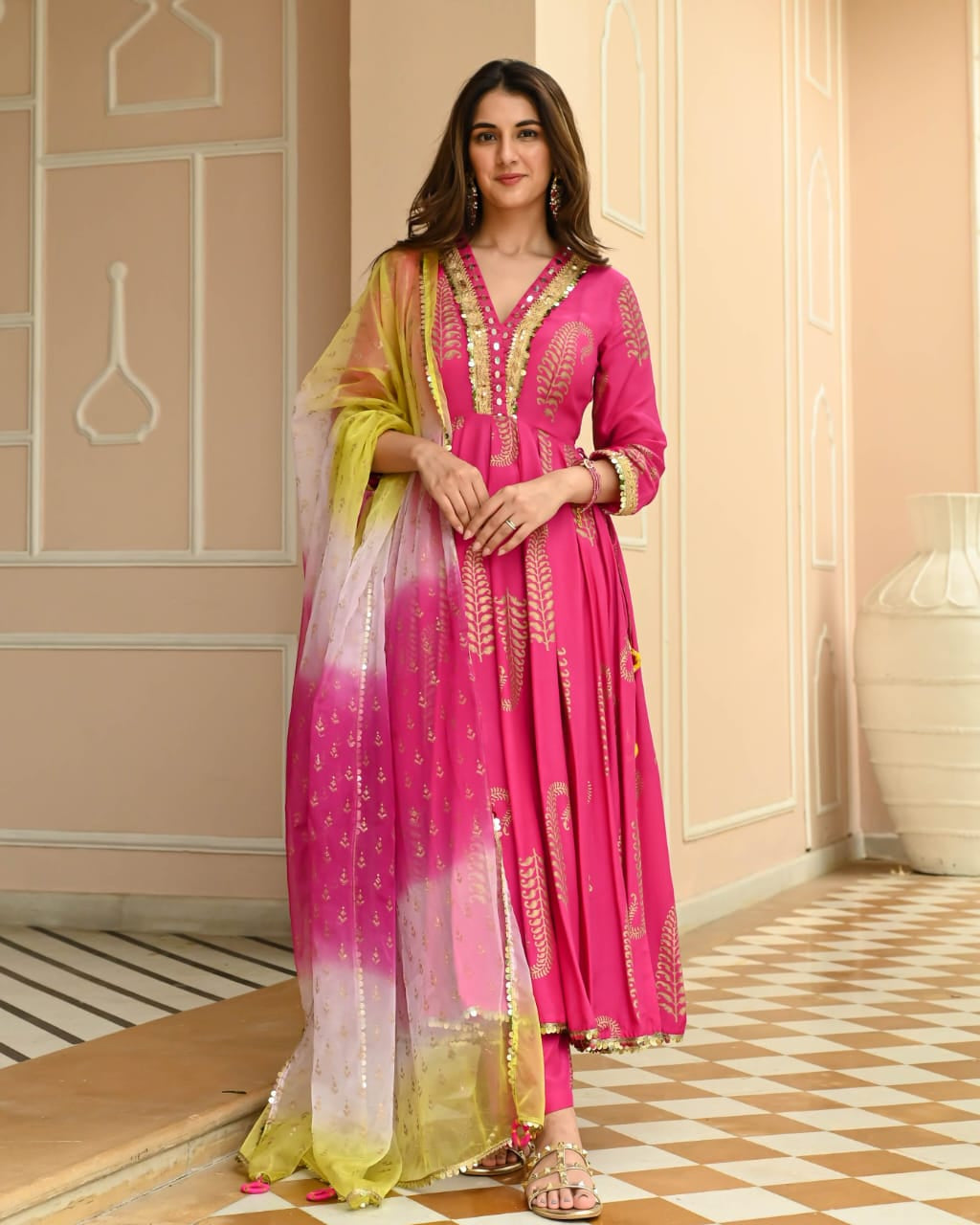 Woman in a pink and yellow traditional outfit standing in a decorated room.