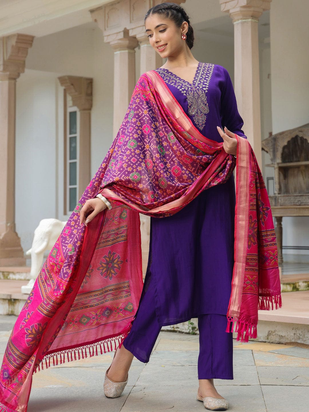 Woman in a traditional outfit with a purple top and pink dupatta in an outdoor setting.