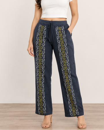 A woman modeling a pair of dark navy wide-leg pants with vertical yellow and white patterned side panels, paired with a white crop top against a neutral studio background.