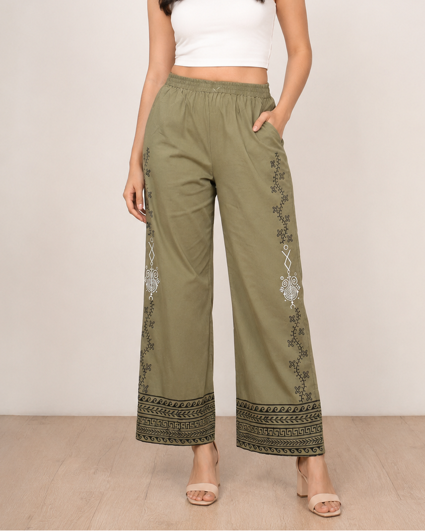 A model wearing olive green wide-leg pants with white and black embroidered details down the sides and at the hem, paired with a white crop top and beige heeled sandals.