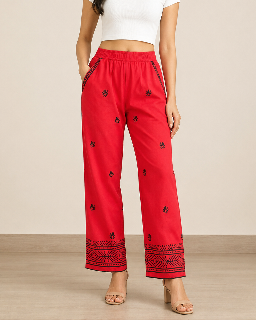 A woman modeling red wide-leg cropped pants with black embroidered floral details and a black patterned hem, paired with a white crop top against a beige studio background.