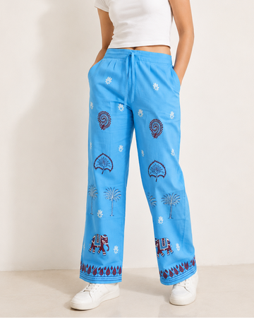 A woman modeling bright blue wide-leg pajama pants with a white crop top and white sneakers against a plain beige studio background.